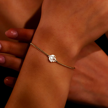 A close-up image of a person's wrist wearing a gold-filled bracelet with a block monogram initial pendant.