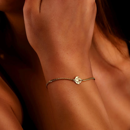 A close-up image of a person's wrist wearing a gold-filled bracelet with a block monogram initial pendant.