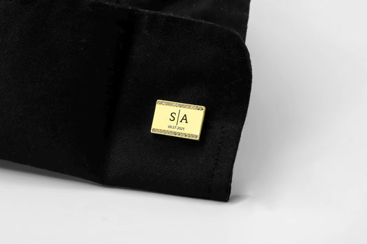 Black fabric with a gold cufflink featuring initials and text on a white background