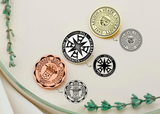 A collection of silver brooches with personalized college emblems, displayed on a white surface with a green floral decoration.