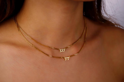 A close-up image of a person wearing a layered gold intertwined necklace with the numbers '833' and '711' on small, dainty chain links.