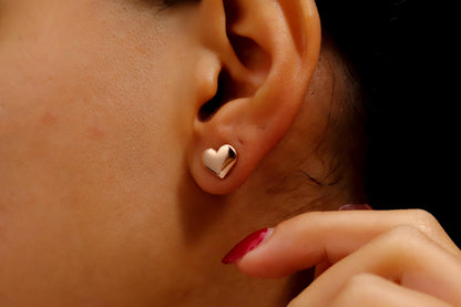 A close-up image of a woman's ear wearing a silver stud heart-shaped earring.