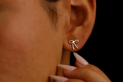 Gold bow-shaped earring worn by a person with a black background