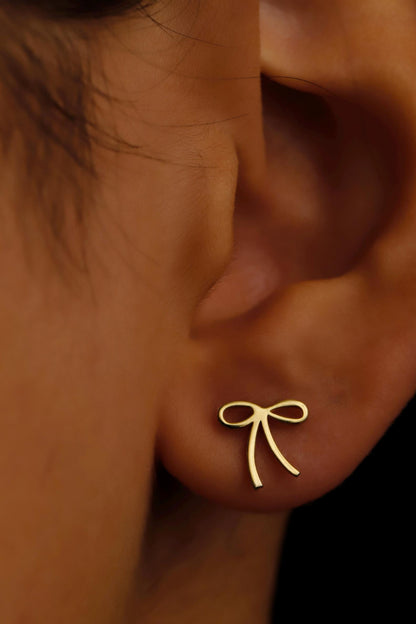 Gold bow-shaped earring on a person's ear with a close-up view.