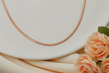 Rose gold snake chain necklace on a white plate with peach roses