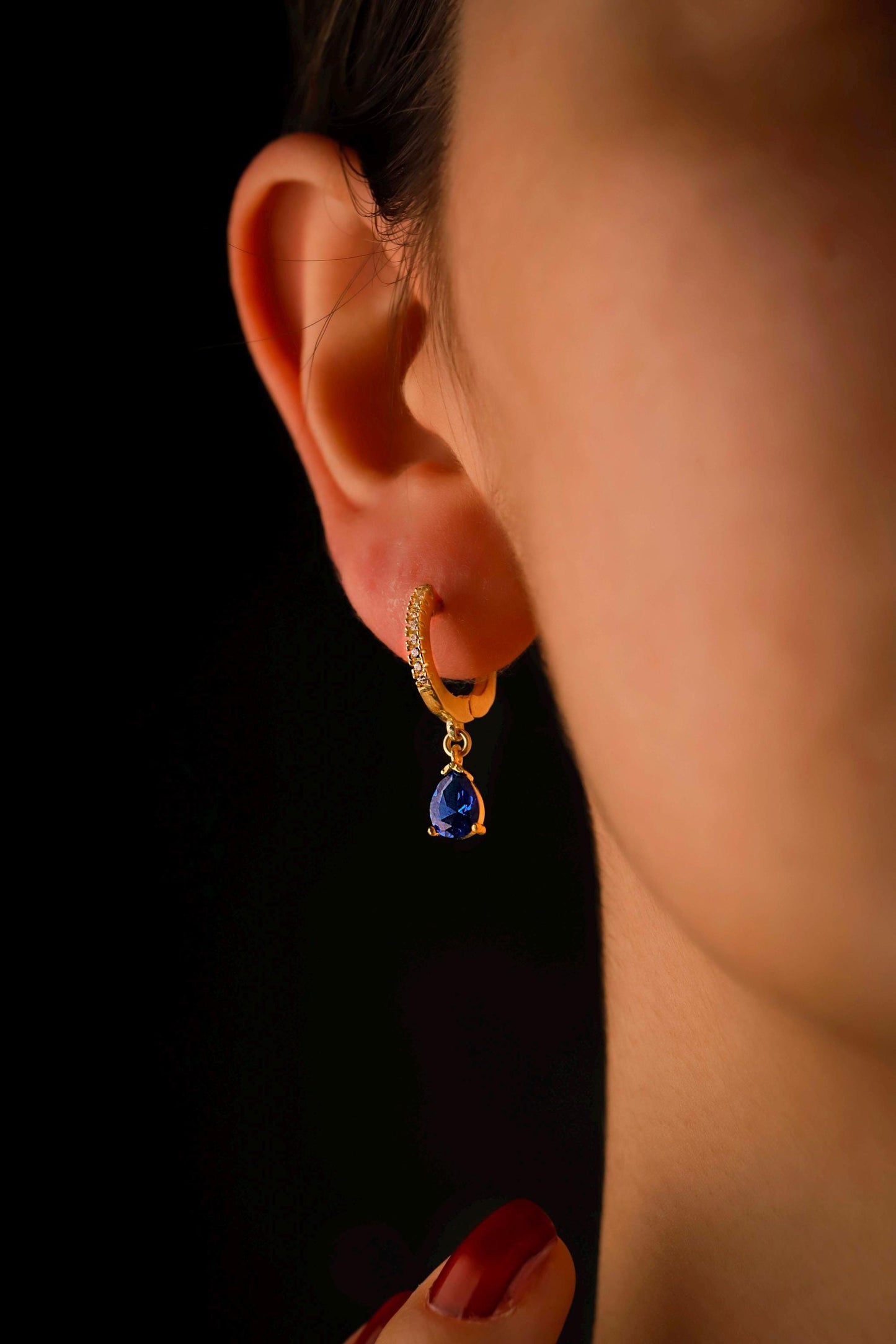 Gold earring with a blue gemstone worn by a person against a dark background