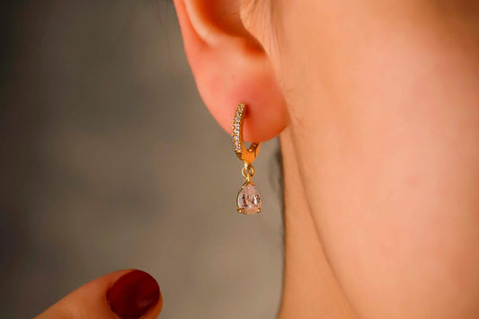 Gold hoop earring with a pink gemstone worn by a person against a neutral background