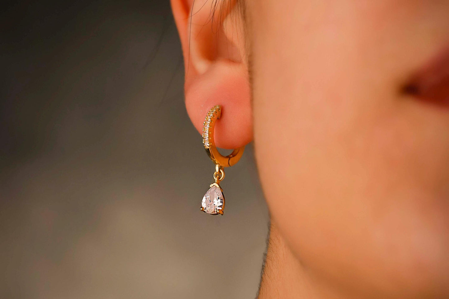 Close-up of a person wearing a gold hoop earring with a heart-shaped pendant.