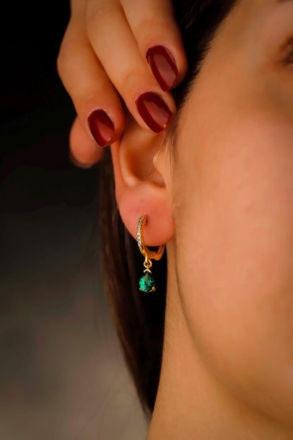 Close-up of a person wearing a gold earring with a green gemstone.