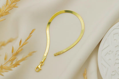 Gold bracelet on a textured beige surface with a decorative plant.