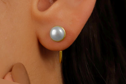 A close-up image of a woman's ear wearing a gold-colored earring with a single pearl.