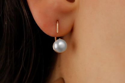 A close-up image of a woman's ear wearing a gold-colored earring with a single pearl.