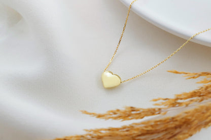 A close-up image of a a dainty silver necklace with a 3D moveable heart pendant in gold color.