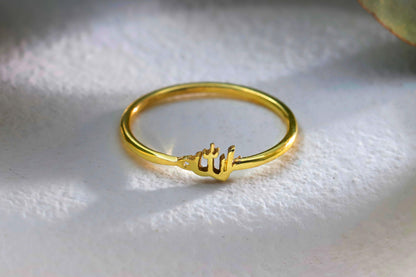 A close-up image of a gold and silver colored ring with Arabic lettering on it