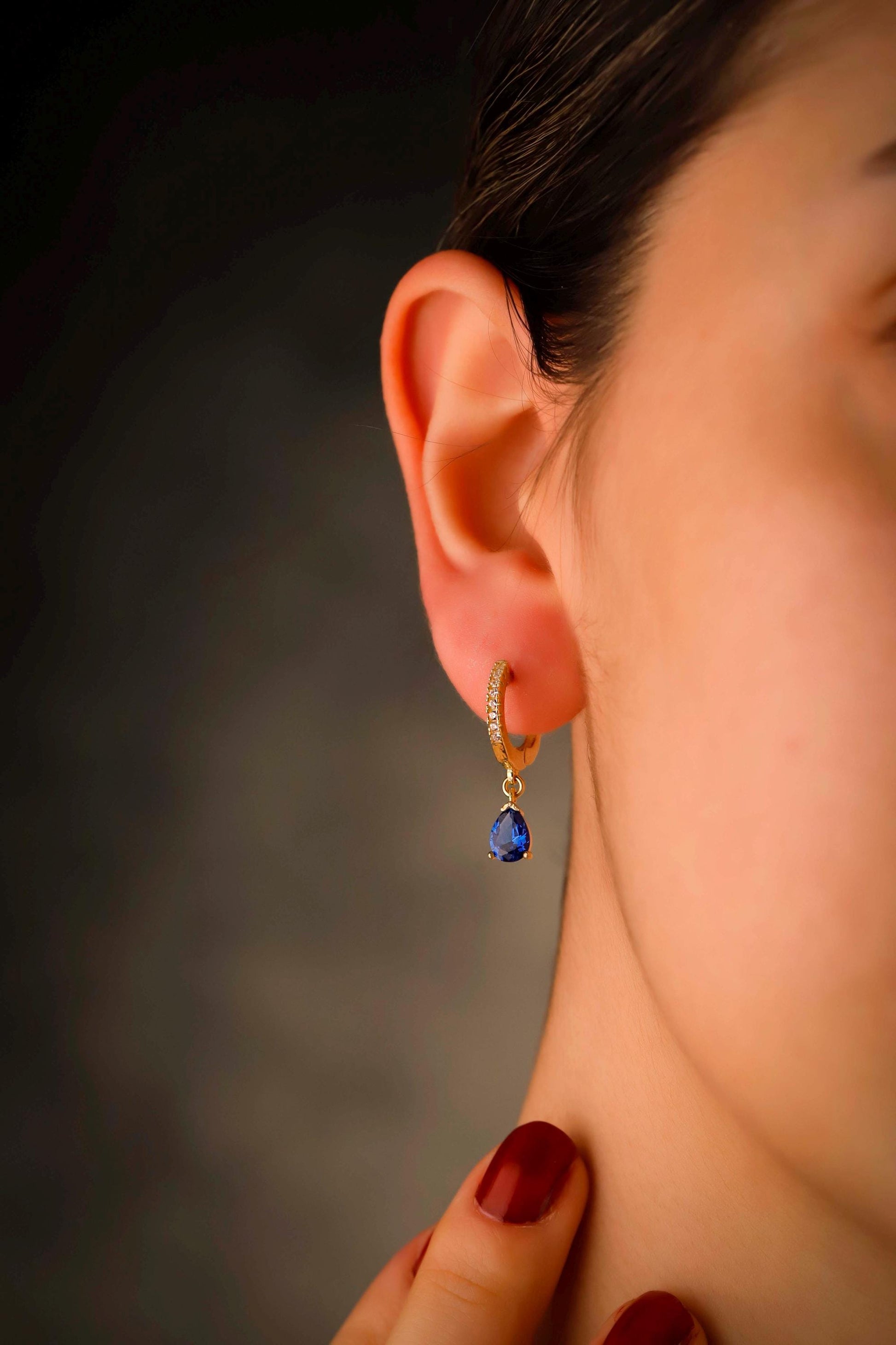 Close-up of a person wearing a gold hoop earring with a blue gemstone against a blurred background