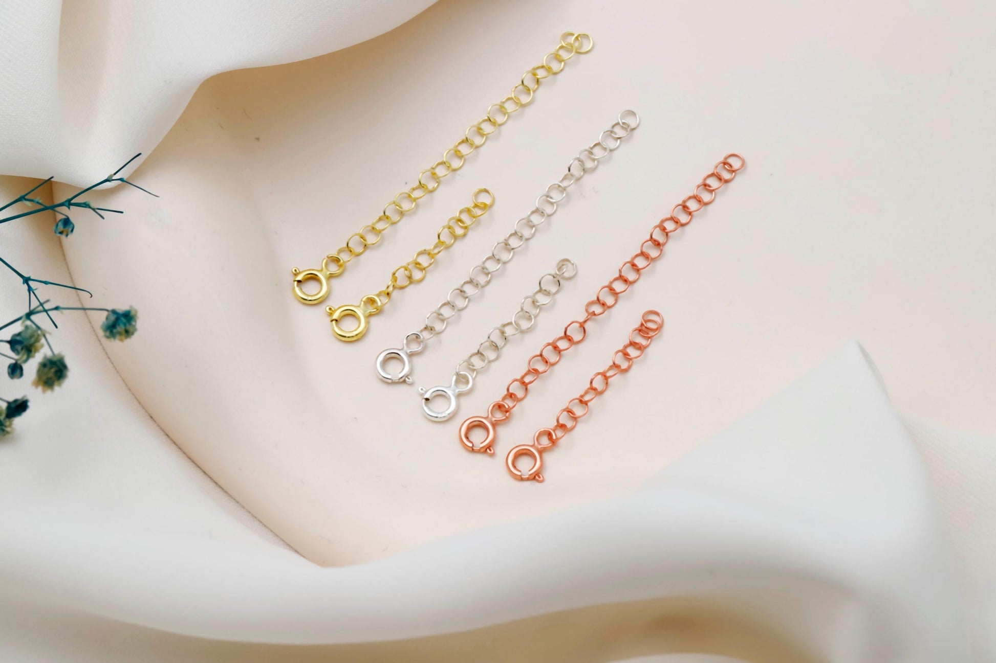 Three gold, silver, and rose gold chain extensions on a light background