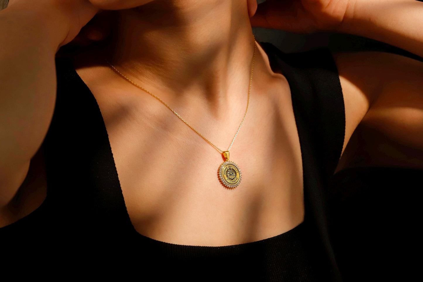 Gold necklace with a pendant on a person wearing a black top.