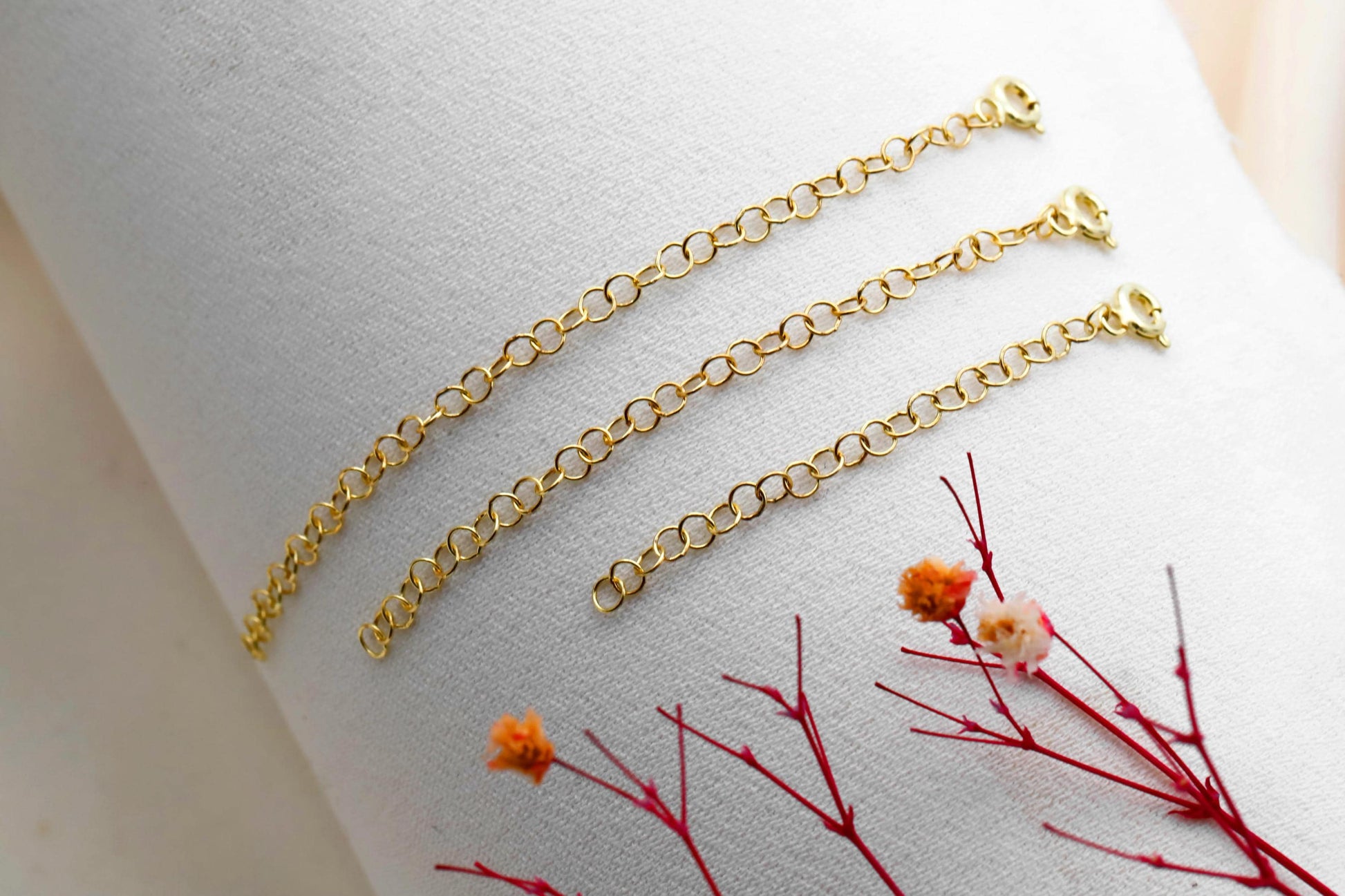 Three adjustable extender chains in gold, silver, and rose gold colors laid out on a marble surface with a decorative flower in the background.