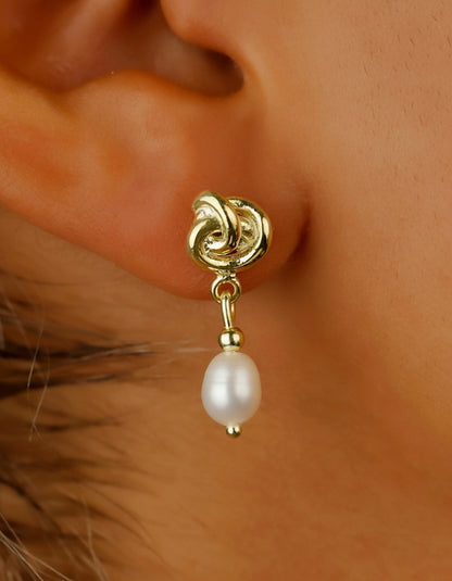 Gold earring with a pearl drop worn on an ear