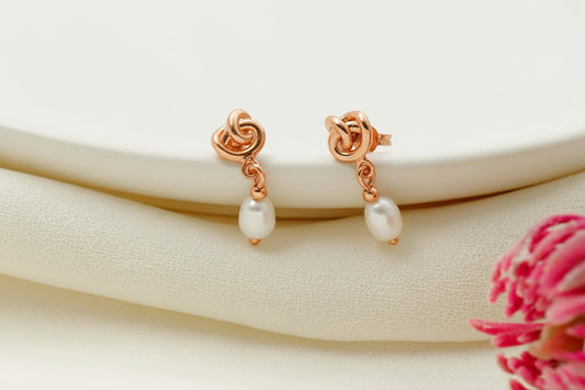 Rose gold earrings with pearl drops on a white surface with a pink flower.