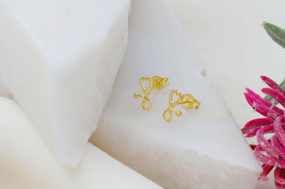 Gold bow-shaped earrings on a white surface with a pink flower.