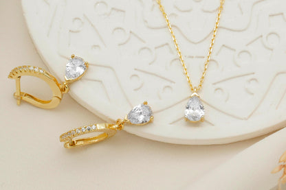 Gold jewelry set with earrings and a necklace on a textured white surface