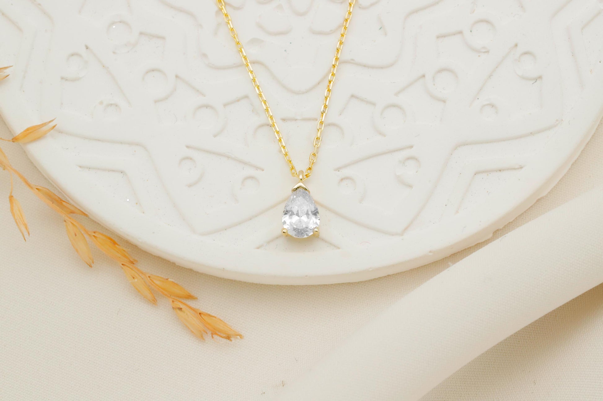 Gold necklace with a clear pendant on a textured white surface