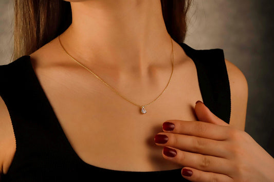 Woman wearing a gold necklace with a pendant, against a neutral background