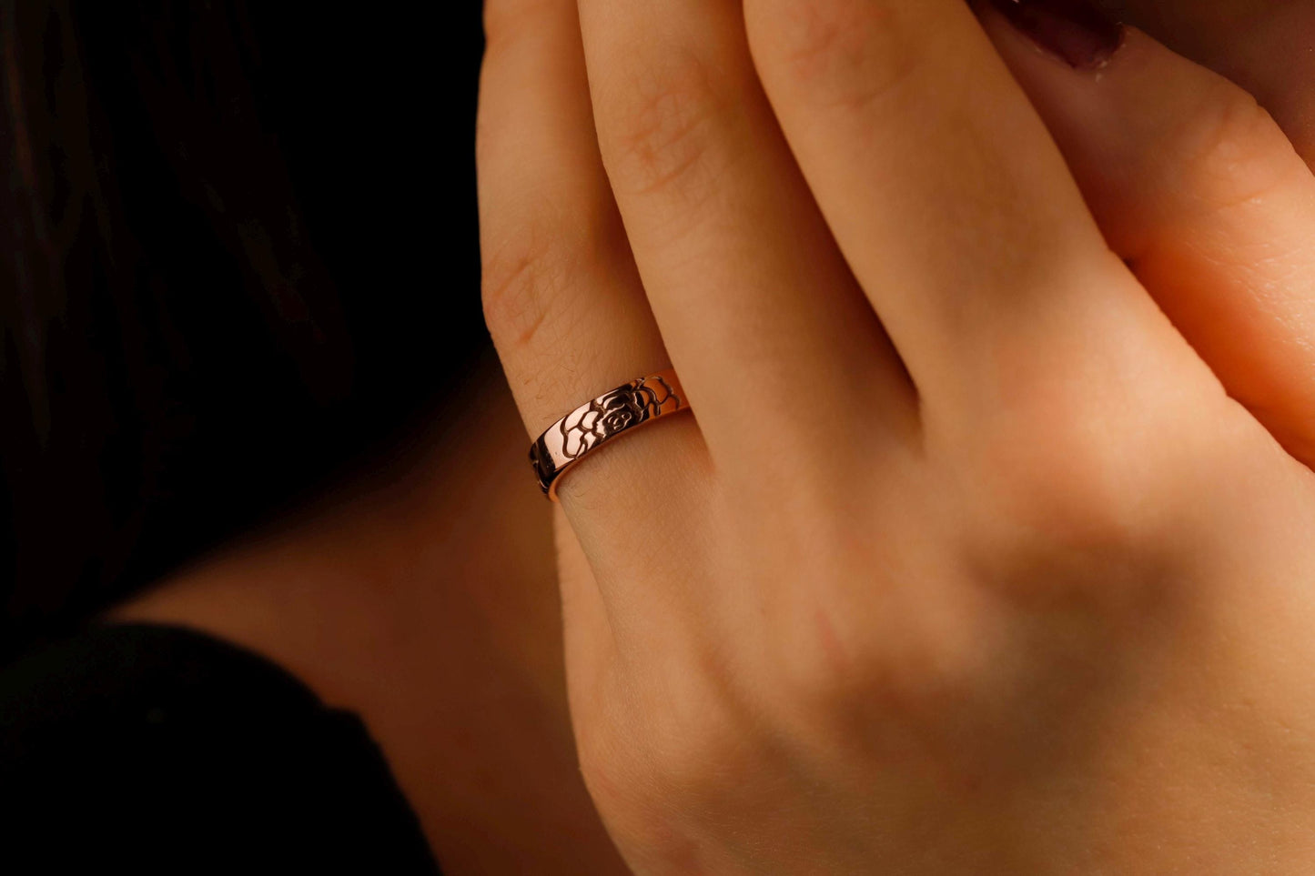 Close-up of a hand wearing a rose gold ring with intricate design.
