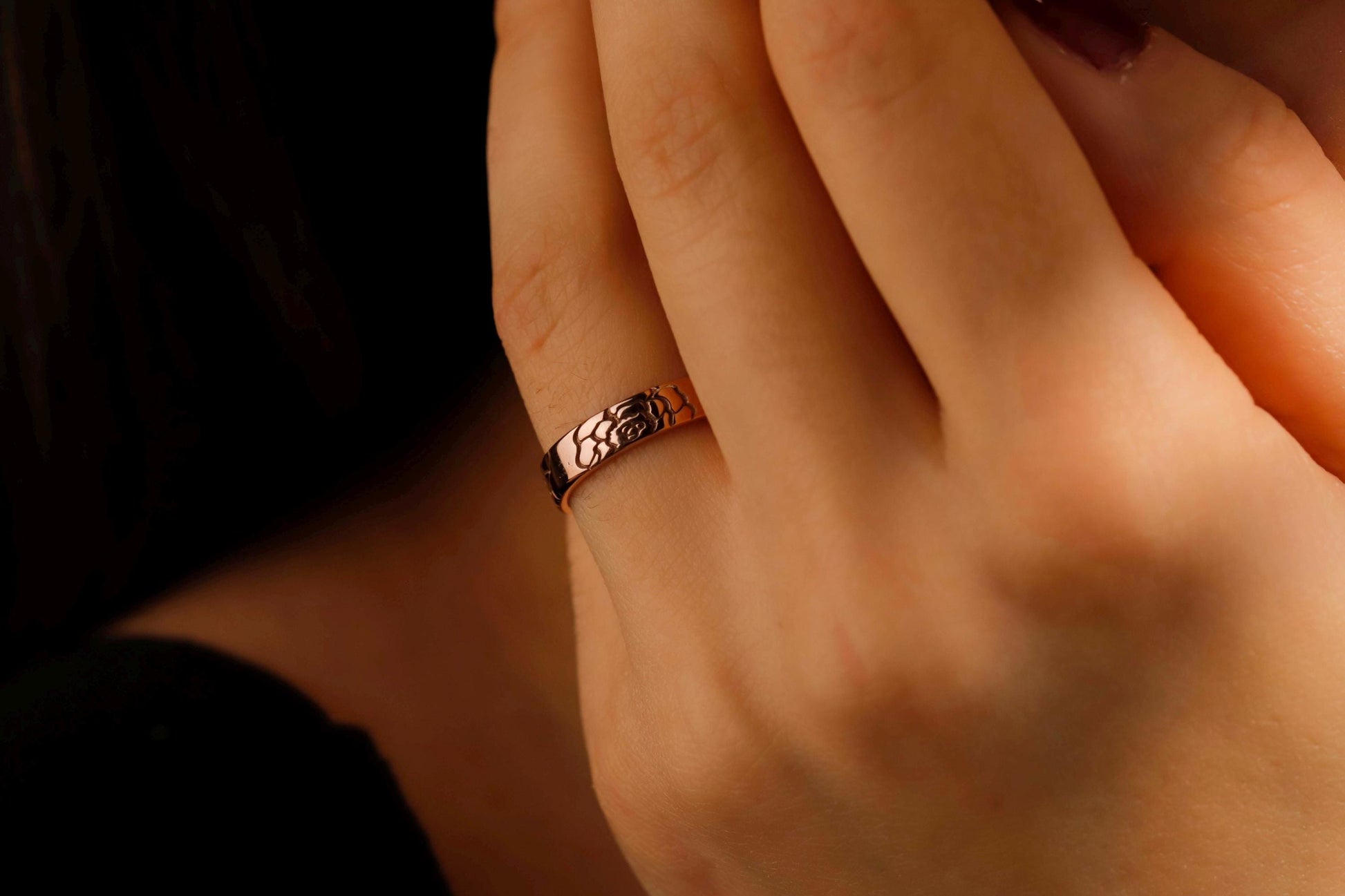 Close-up of a hand wearing a rose gold ring with intricate design.