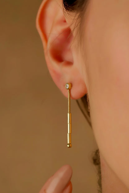 A close-up image of a woman's ear wearing a silver dangle earring with a morse code.