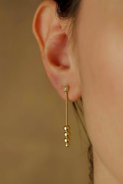 A close-up image of a woman's ear wearing a silver dangle earring with a morse code.