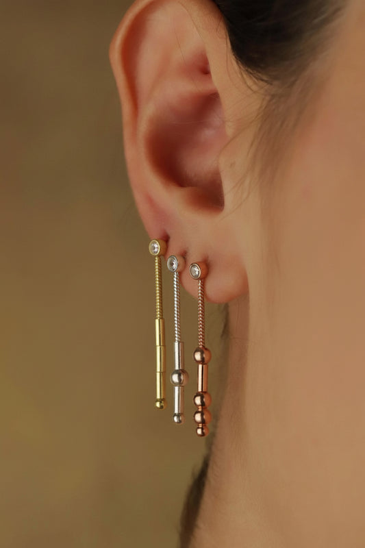 A close-up image of a woman's ear wearing a silver dangle earring with a morse code.