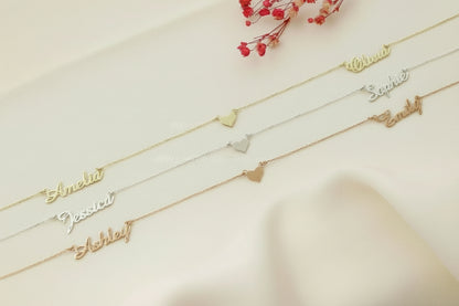 Three gold name bracelets on a light surface with red flowers in the background