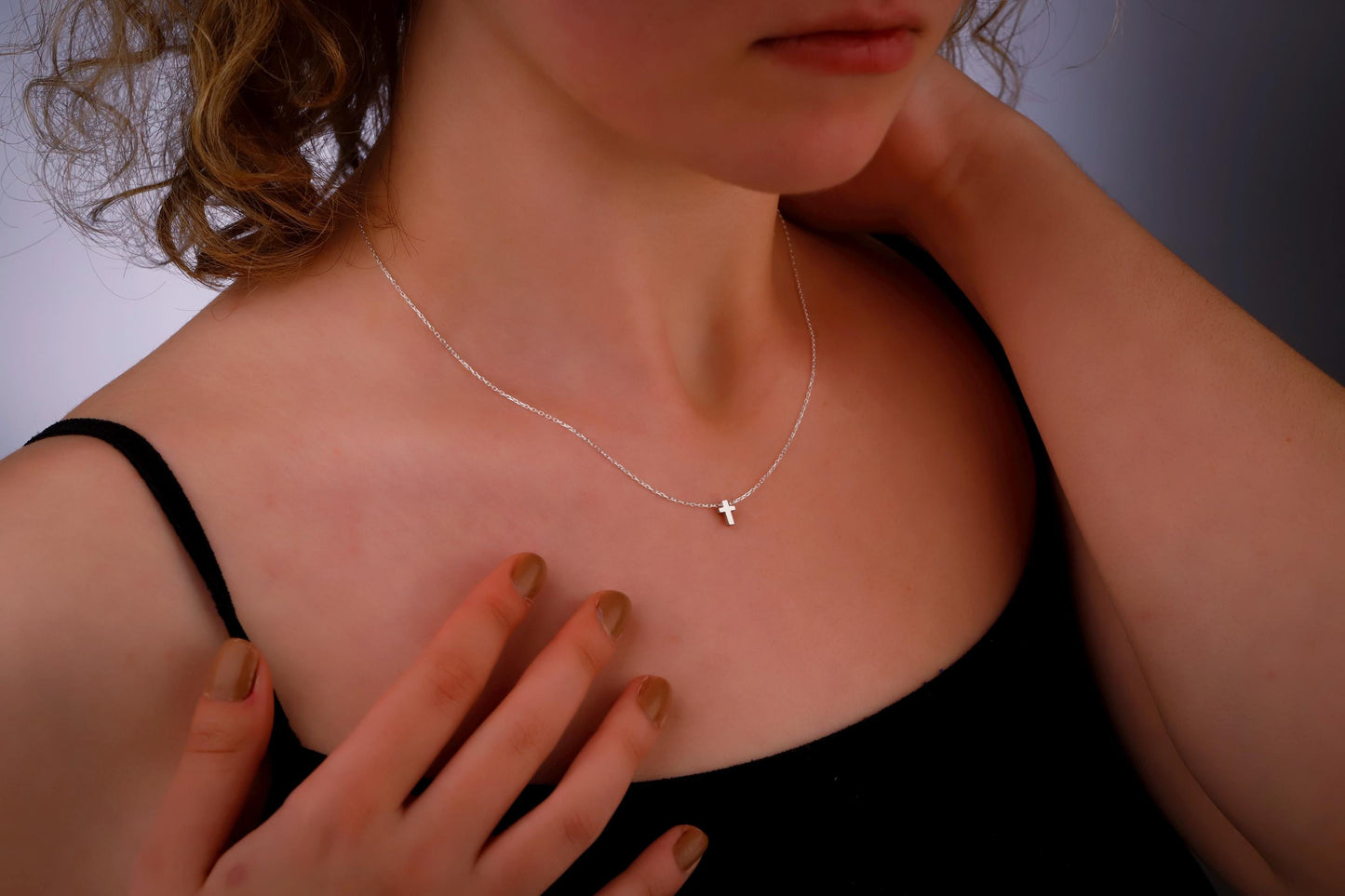 Person wearing a delicate necklace with a small pendant, touching their chest.