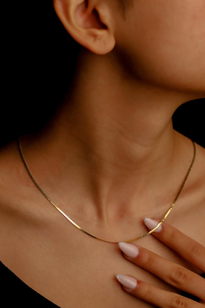 A person wearing a dainty snake chain necklace in gold color.