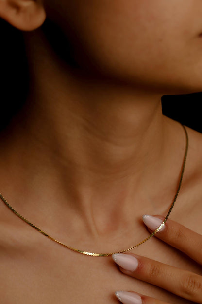 A person wearing a dainty snake chain necklace in gold color.