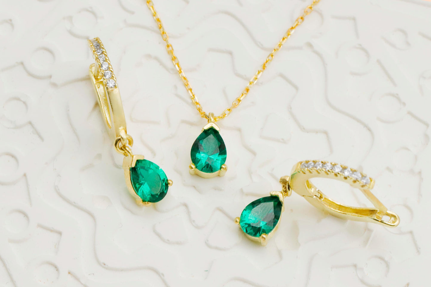 Gold jewelry set with emerald green gemstones on a textured white background
