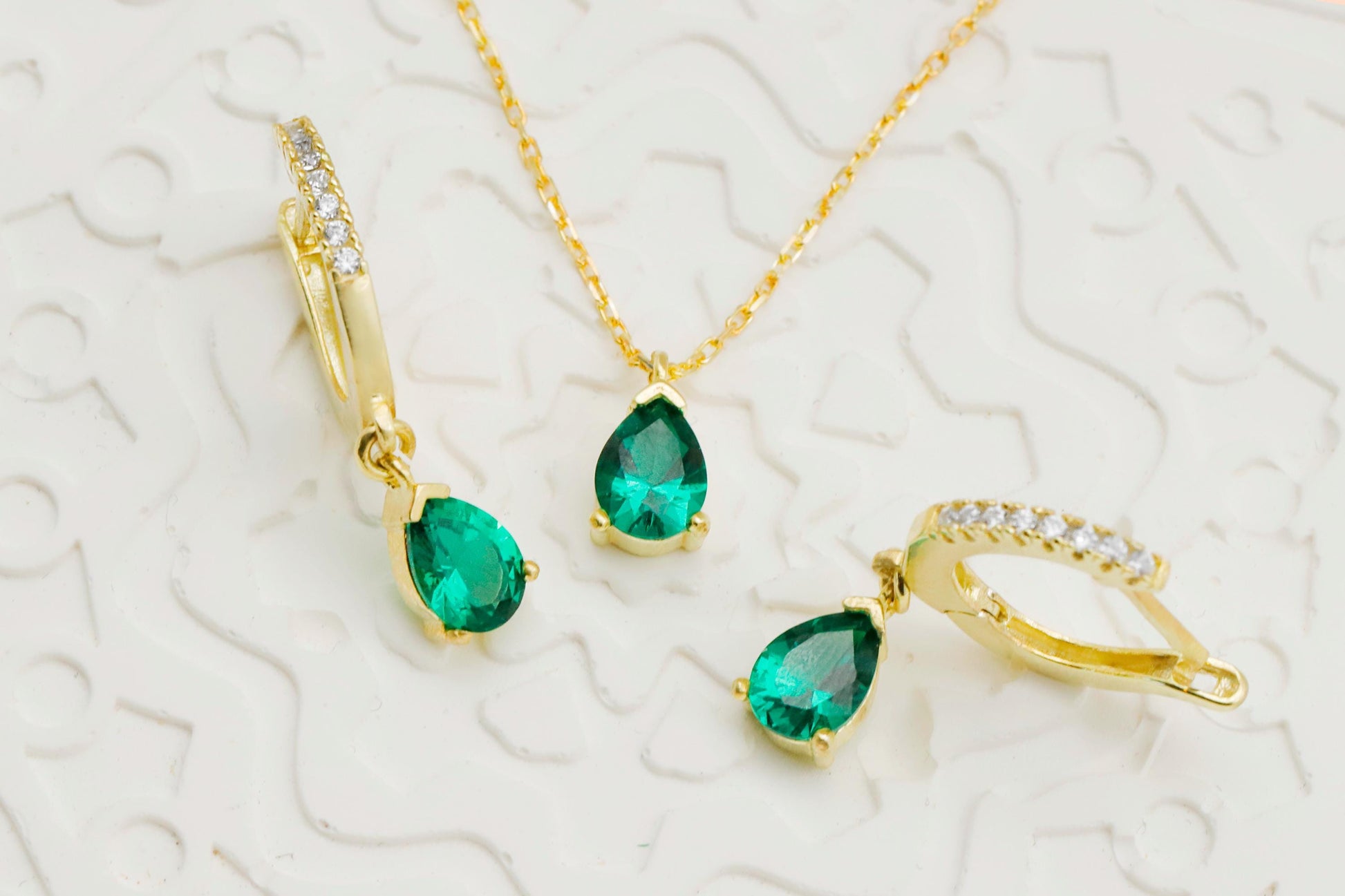 Gold jewelry set with emerald green gemstones on a textured white background