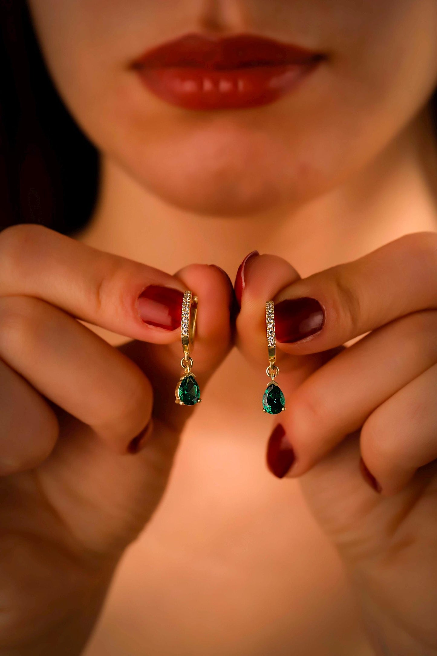 Close-up of a person holding two pairs of green gemstone earrings.