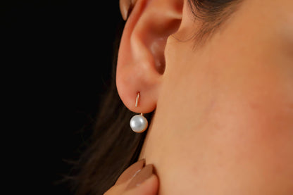 A close-up image of a woman's ear wearing a gold-colored earring with a single pearl.