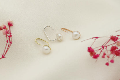 A close-up image of a woman's ear wearing a gold-colored earring with a single pearl.