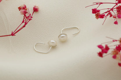 A close-up image of a woman's ear wearing a gold-colored earring with a single pearl.