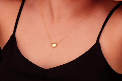 A close-up image of a person wearing a dainty silver necklace with a 3D moveable heart pendant in gold color.