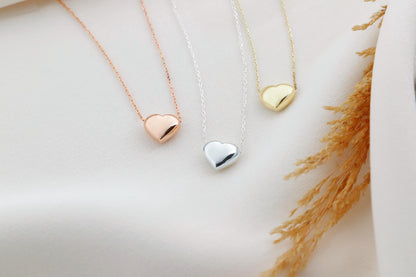 A close-up image of 3 dainty silver necklaces with a 3D moveable heart pendant in gold silver and rose color.
