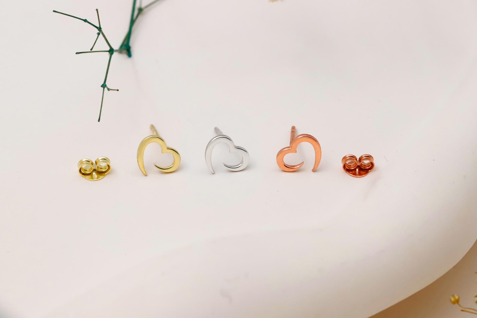 Set of heart-shaped earrings in gold, silver, and rose gold on a white surface.