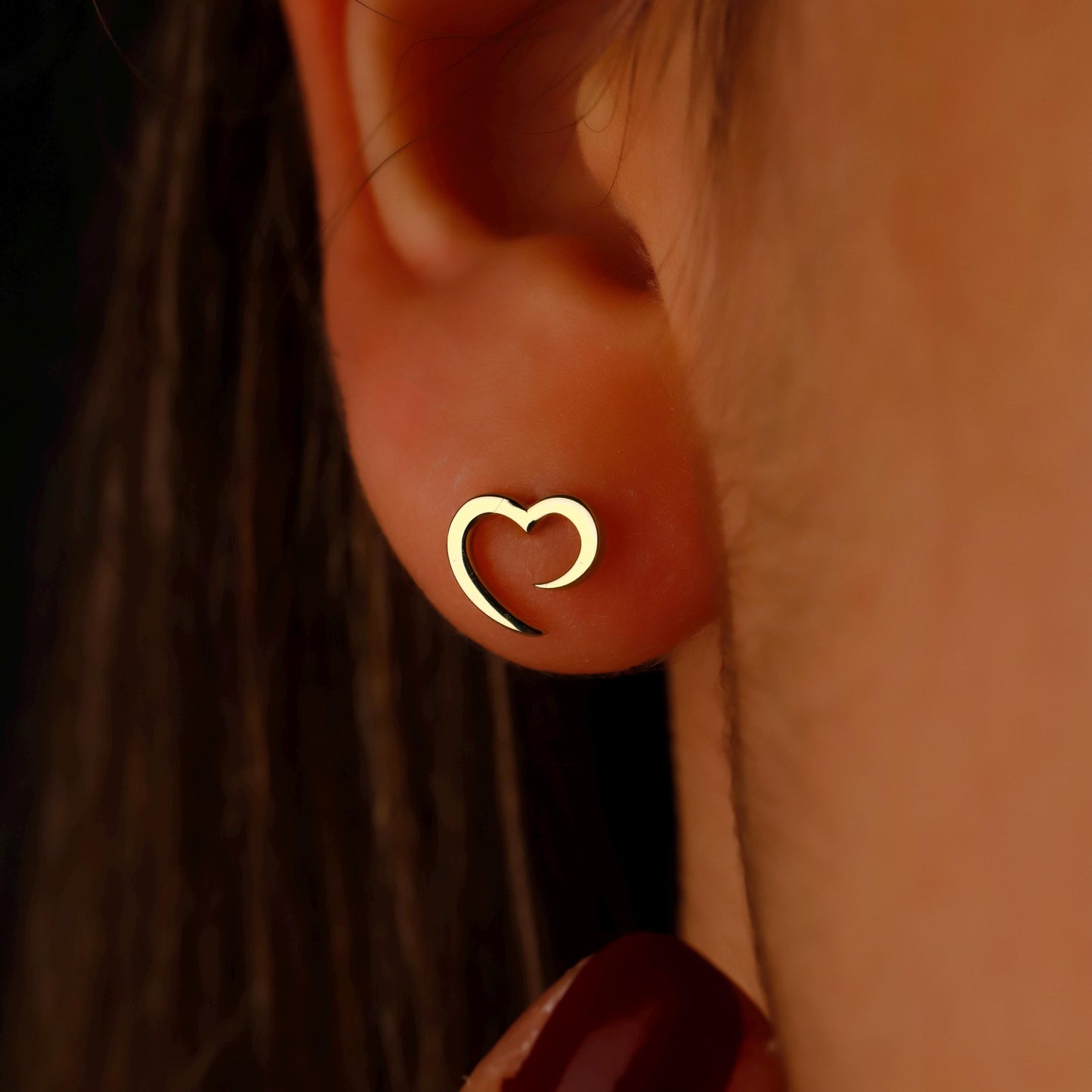 Close-up of an ear wearing a gold heart-shaped earring.