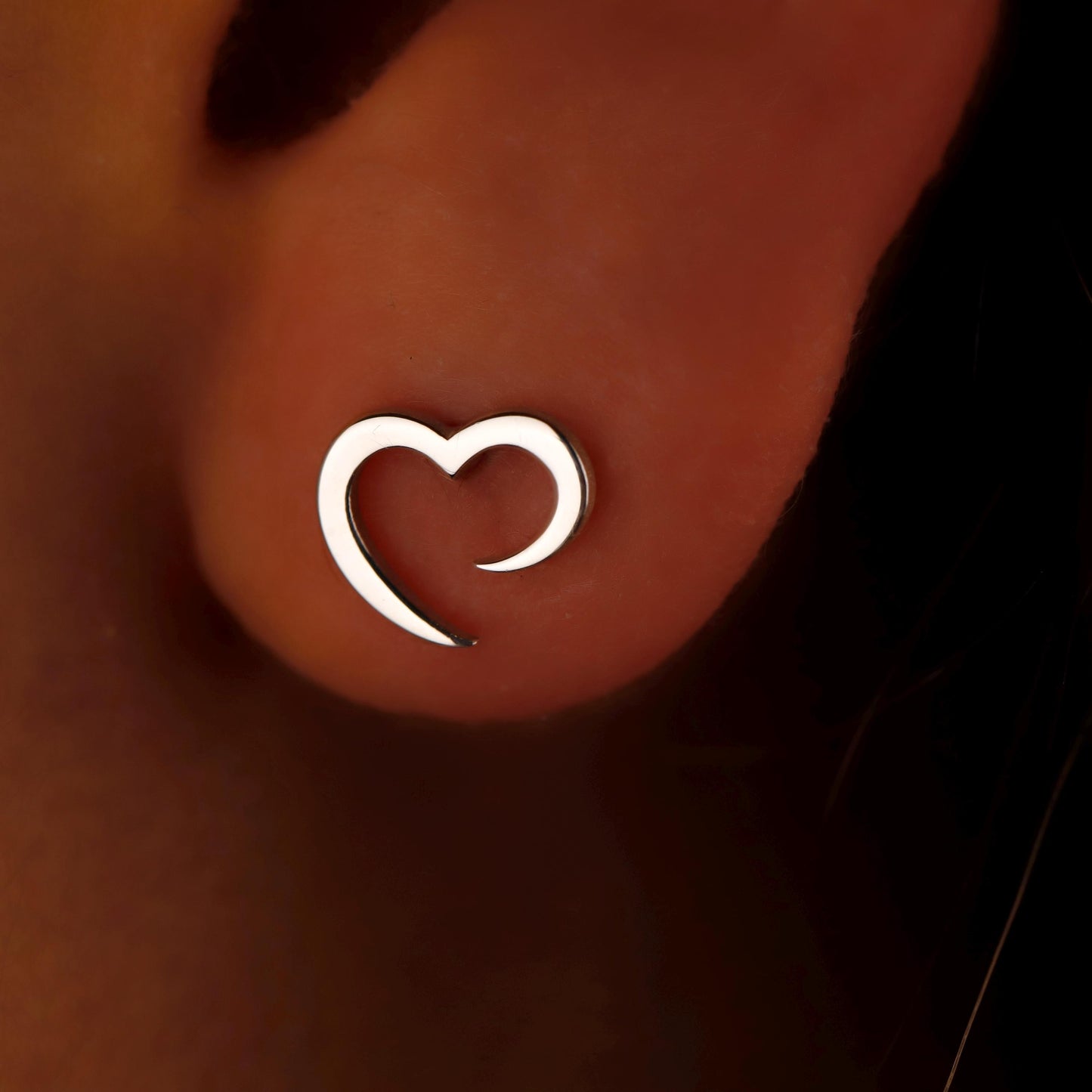 Silver heart-shaped earring on a person's ear