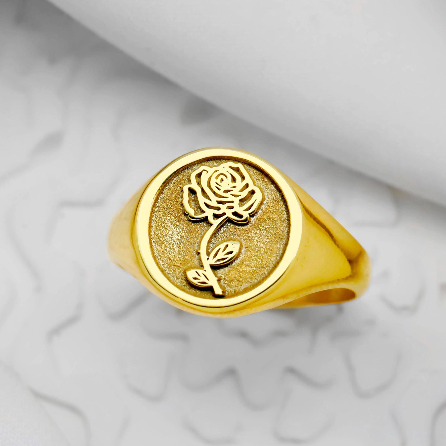Gold ring with rose design on a marble surface