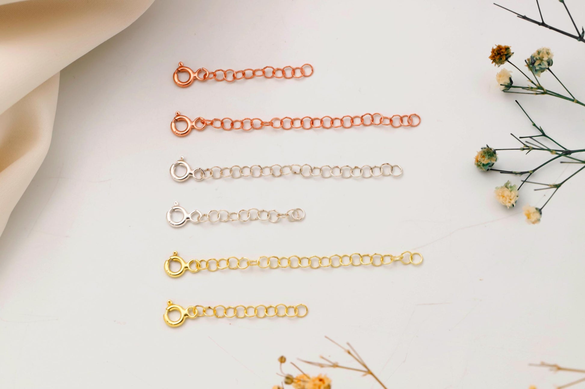 Set of gold necklaces on a light surface with dried flowers.